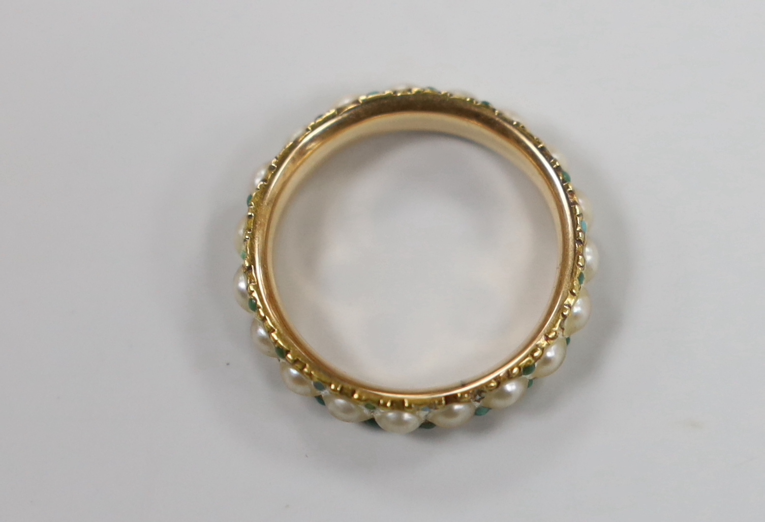 An antique yellow metal and split pearl set full eternity ring with green cabochon spacers, size K/L, gross weight 3 grams.